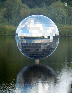 Fotografi av skulpturen Spegelbollen som står i lagunen i Växjö. Bollen består av många små speglar som på ett effektfullt sätt reflekterar ljuset.